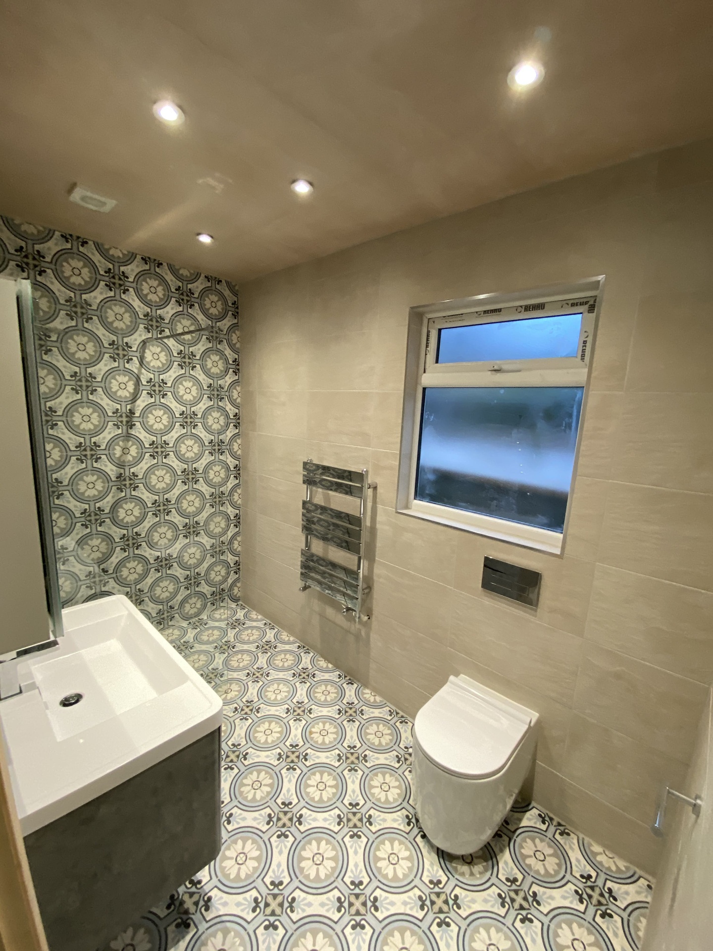 Completed bathroom with patterned floor tiles, feature wall and chrome heated towel rail