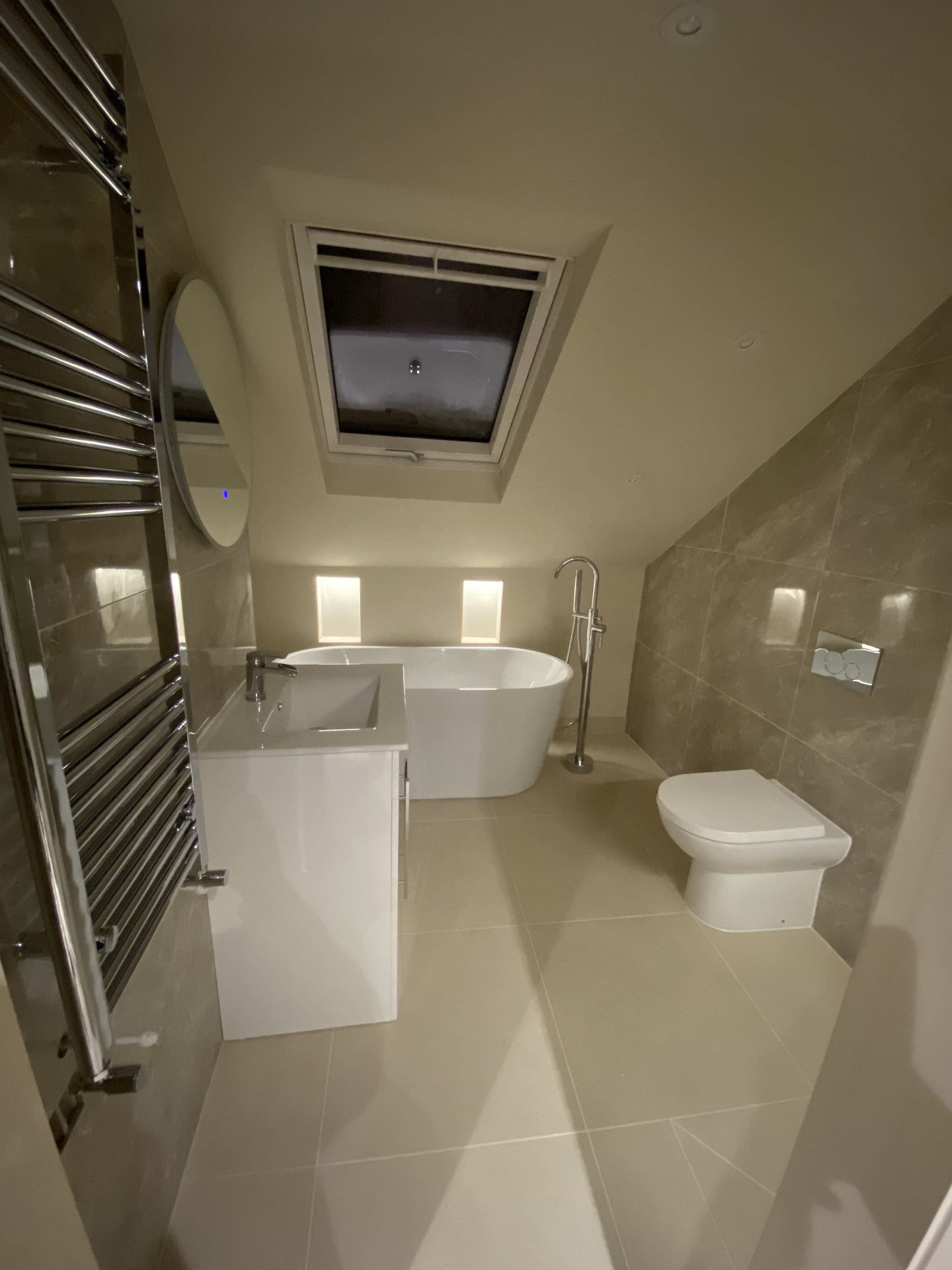 Completed loft bathroom with freestanding bath, rooflight and stone-effect tiling