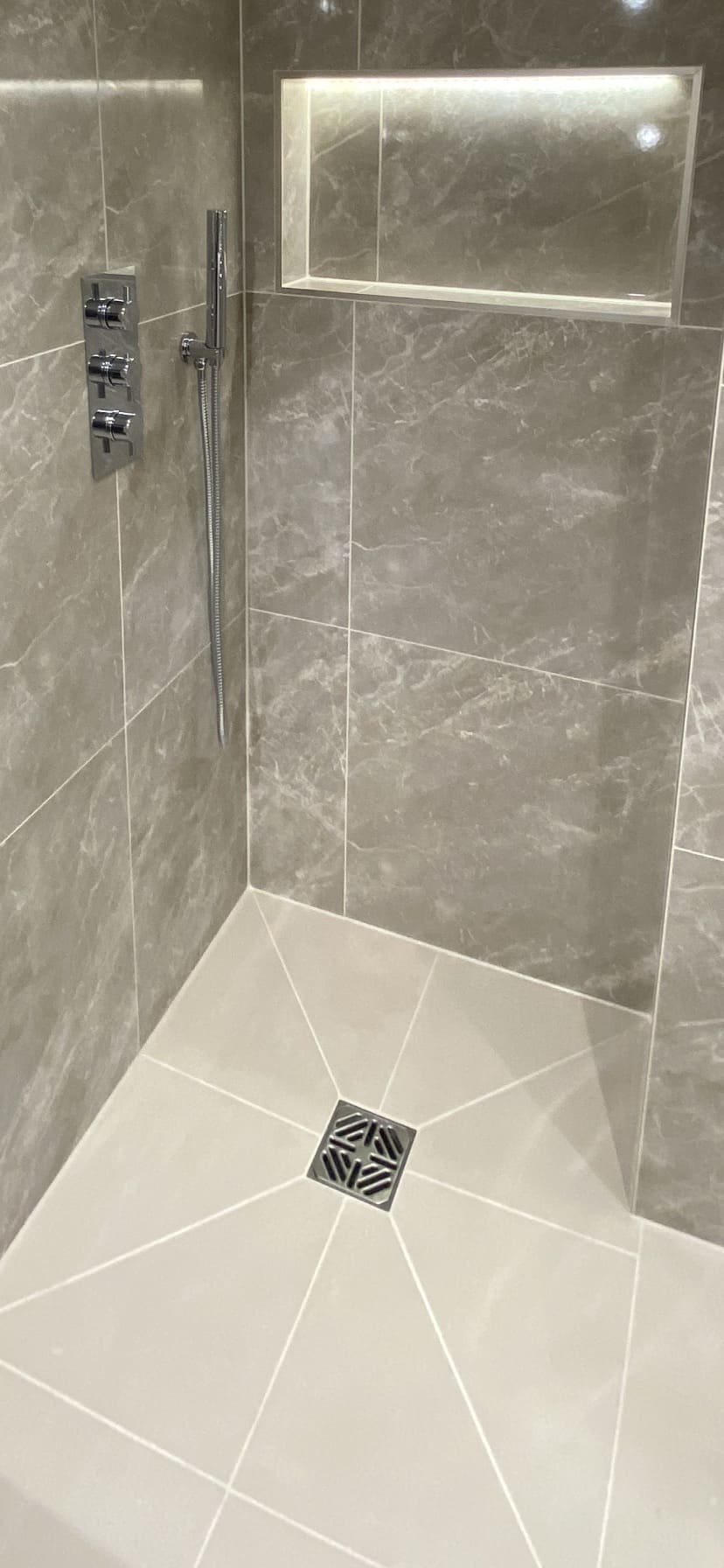 Completed walk-in shower with grey marble-effect tiling and recessed niche