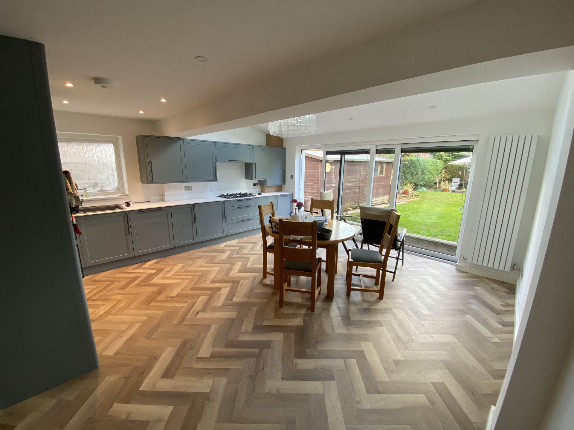Finished grey kitchen extension with herringbone flooring and wide garden doors