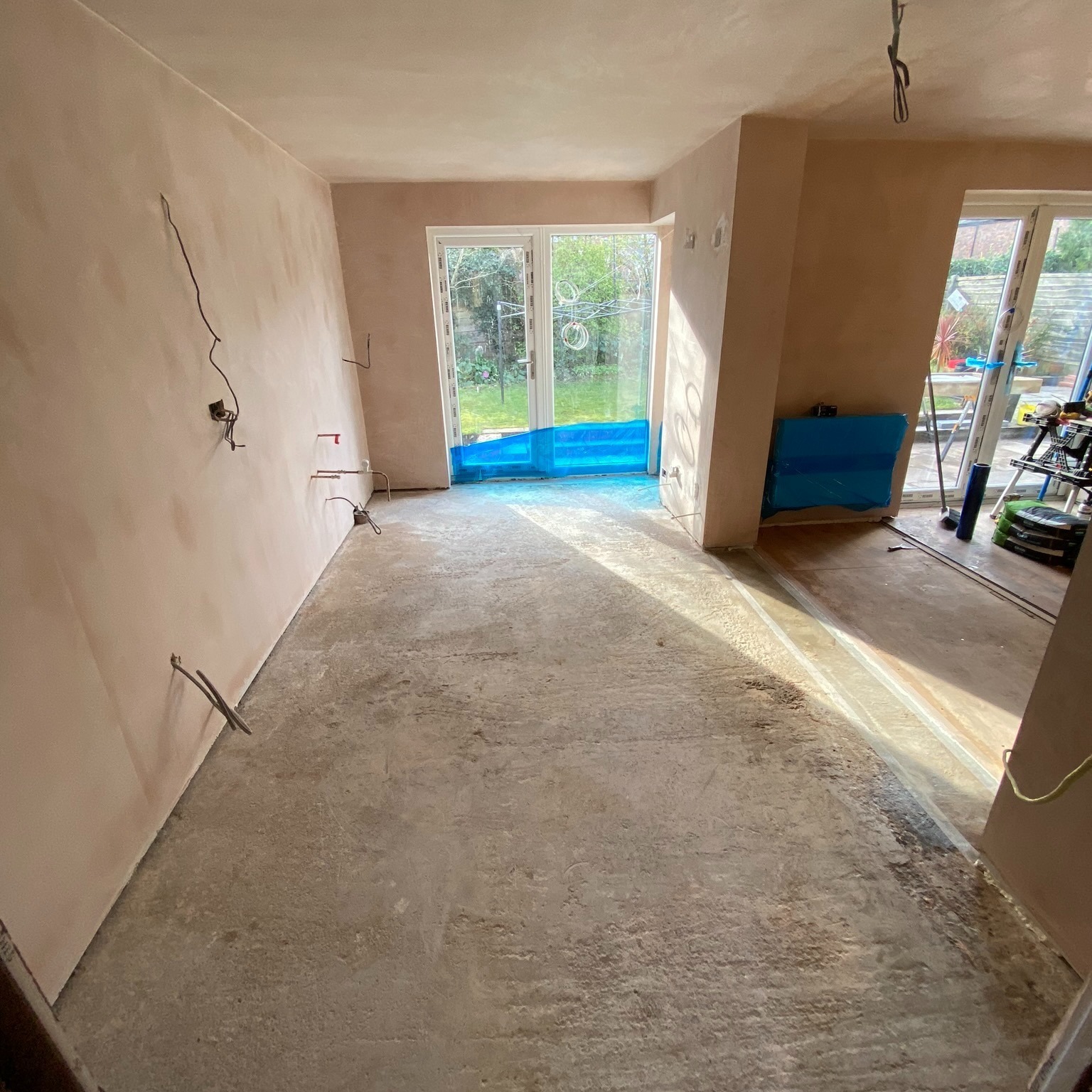 Garage conversion in progress with freshly plastered walls, new patio doors and prepared sub-floor ready for finishes