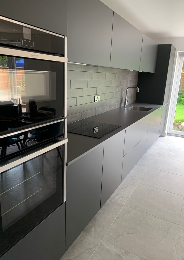 Completed graphite handleless kitchen with integrated Neff appliances, stone worktops and large-format porcelain flooring