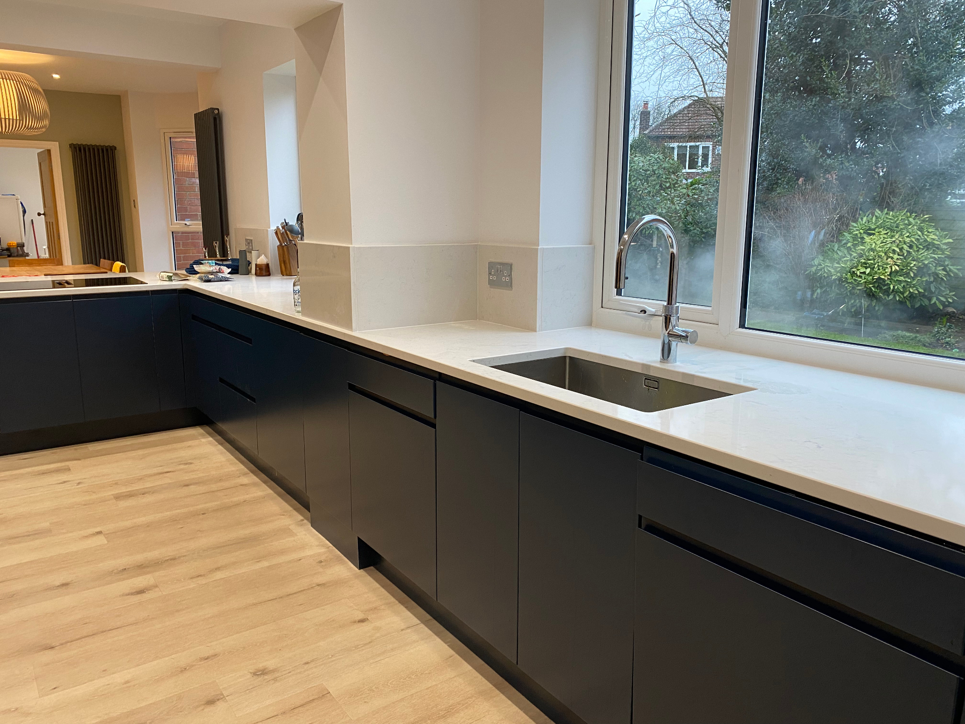 Completed handleless navy kitchen with white quartz worktops, undermount sink and large picture window to garden